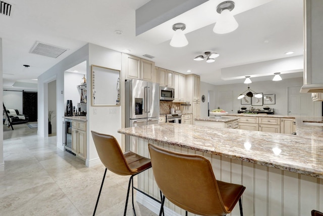 kitchen with appliances with stainless steel finishes, decorative light fixtures, light stone countertops, and cream cabinets