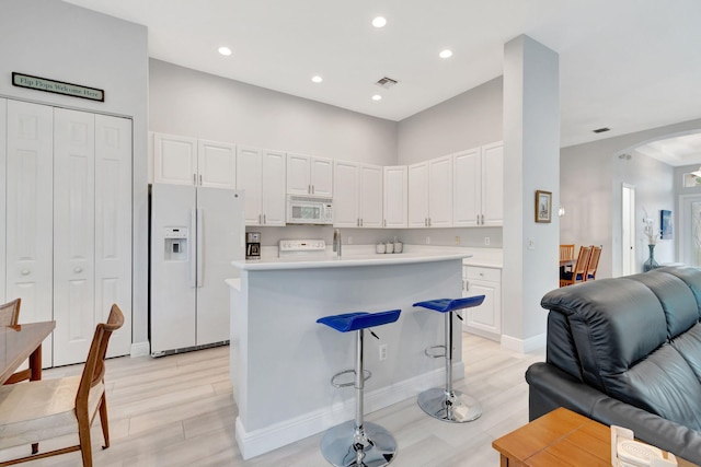 kitchen with white appliances, light hardwood / wood-style floors, white cabinetry, a kitchen breakfast bar, and a center island with sink