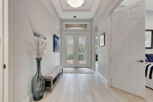 foyer featuring a raised ceiling, light wood-type flooring, and french doors