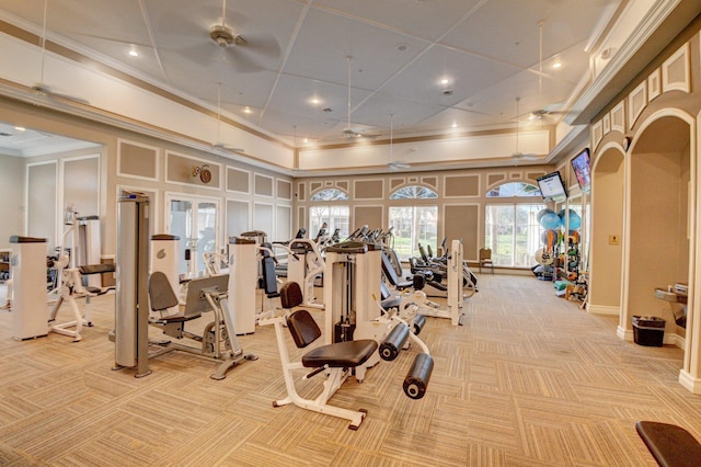 gym with a towering ceiling, light colored carpet, crown molding, and ceiling fan