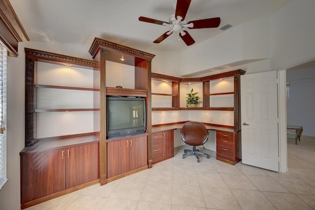 unfurnished office with built in desk, light tile patterned floors, and ceiling fan