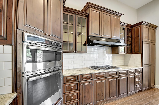 kitchen with light stone countertops, decorative backsplash, stainless steel appliances, and light hardwood / wood-style flooring