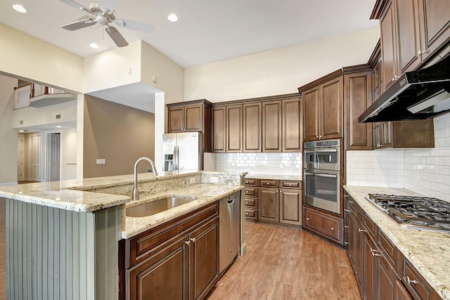 kitchen featuring sink, light stone counters, light hardwood / wood-style floors, a center island with sink, and appliances with stainless steel finishes