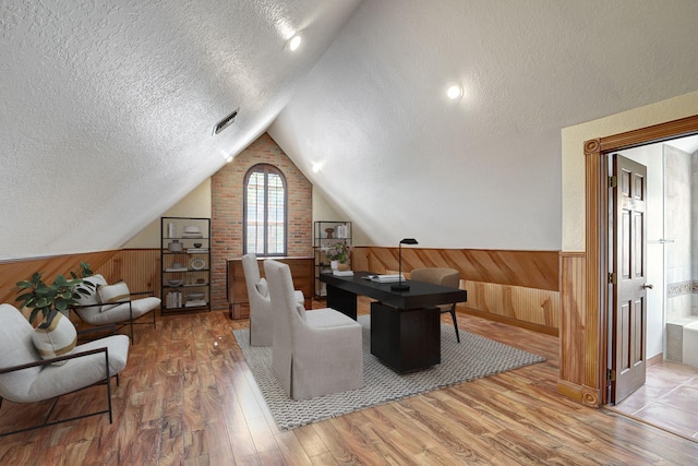 interior space with hardwood / wood-style flooring, wood walls, lofted ceiling, and a textured ceiling