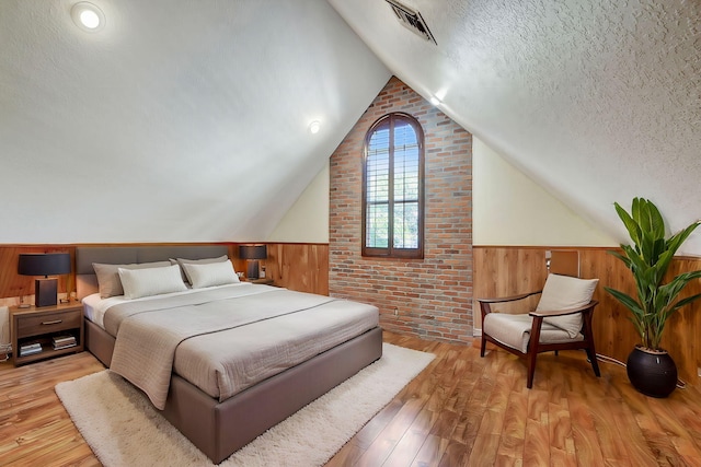 bedroom with lofted ceiling, wood walls, light hardwood / wood-style floors, and a textured ceiling