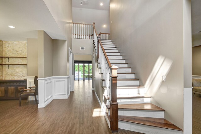 staircase with a stone fireplace, hardwood / wood-style floors, and a towering ceiling