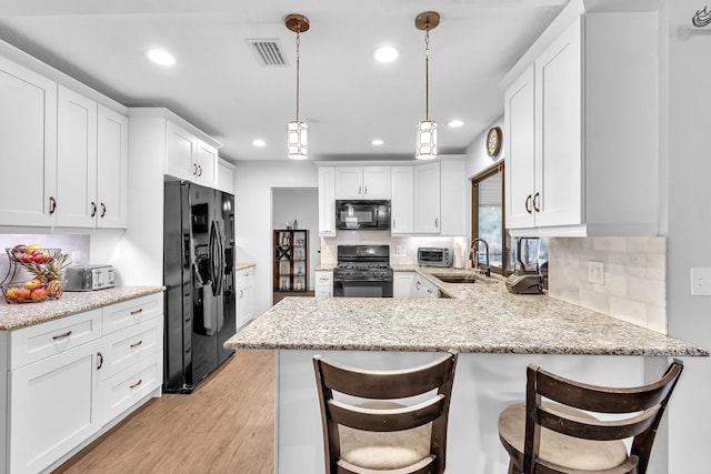 kitchen featuring decorative light fixtures, black appliances, a breakfast bar area, and light hardwood / wood-style flooring