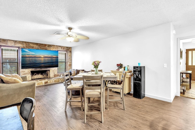 dining area featuring a fireplace, a textured ceiling, ceiling fan, and wood-type flooring