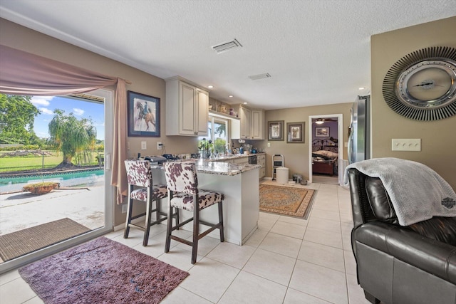 kitchen with light stone counters, light tile patterned floors, a textured ceiling, a kitchen breakfast bar, and cream cabinets