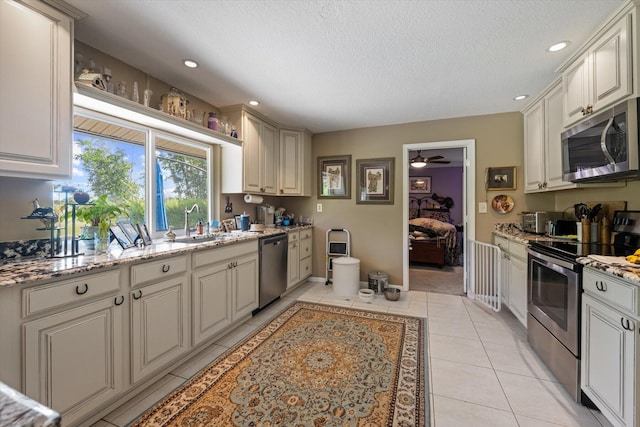 kitchen featuring light tile patterned flooring, ceiling fan, sink, light stone counters, and appliances with stainless steel finishes