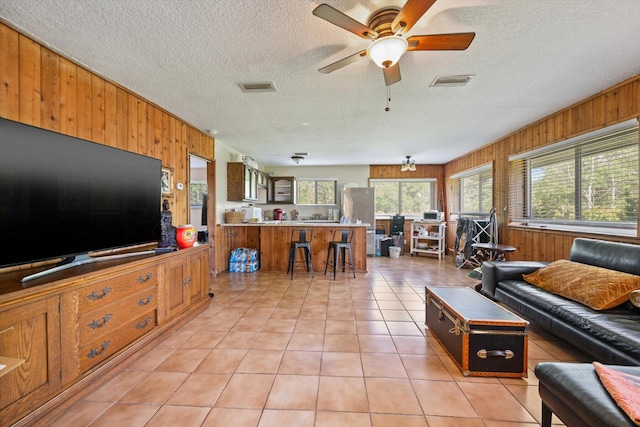 living room with ceiling fan, a textured ceiling, wooden walls, and light tile patterned floors