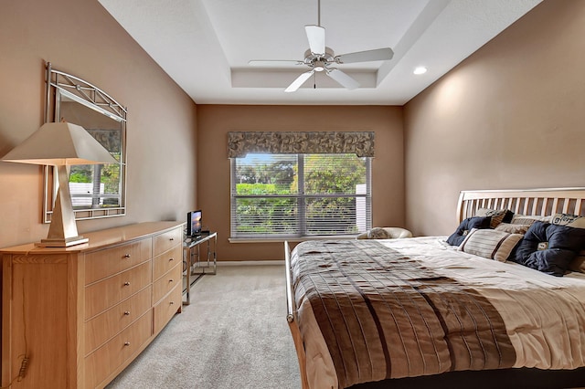 bedroom featuring ceiling fan, light colored carpet, and a tray ceiling