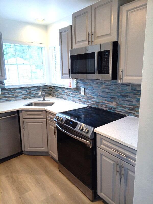 kitchen with appliances with stainless steel finishes, light hardwood / wood-style flooring, tasteful backsplash, and sink