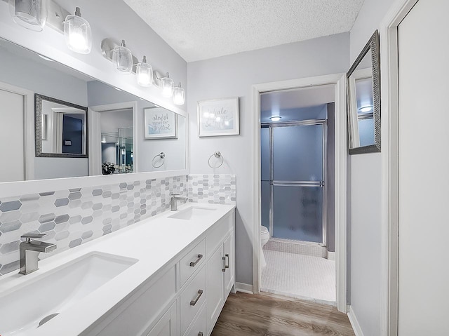 bathroom featuring toilet, hardwood / wood-style flooring, decorative backsplash, an enclosed shower, and a textured ceiling