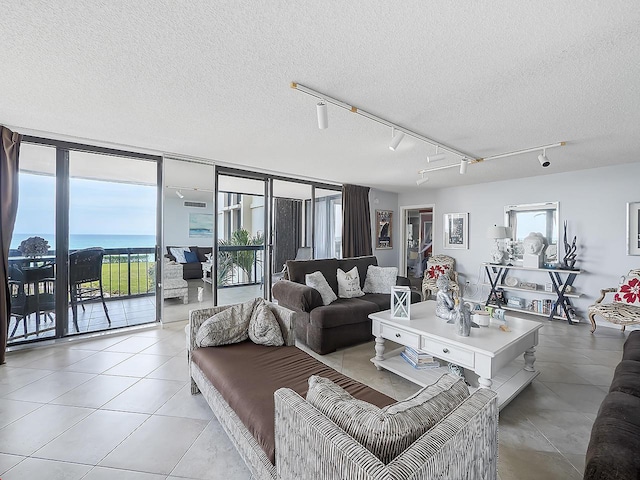 living room with a textured ceiling, light tile patterned floors, a wall of windows, and a water view