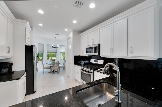 kitchen featuring appliances with stainless steel finishes, white cabinetry, sink, dark stone countertops, and hanging light fixtures