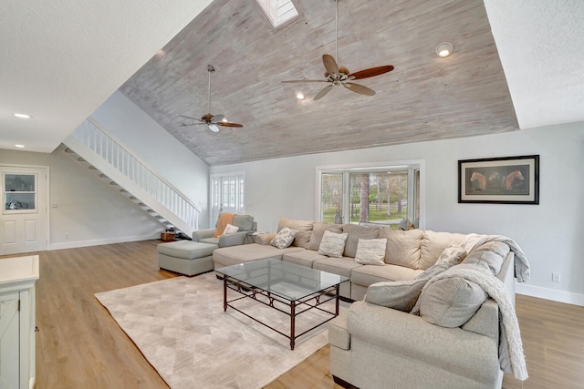 living room with light wood-type flooring, ceiling fan, a skylight, and a textured ceiling