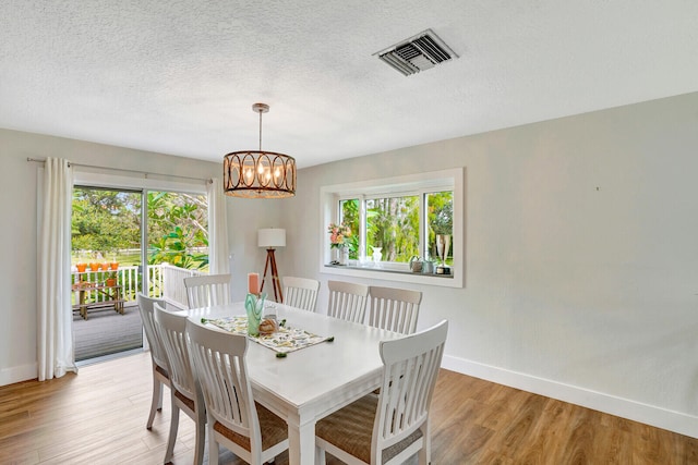 dining area featuring a textured ceiling, light hardwood / wood-style flooring, and a notable chandelier