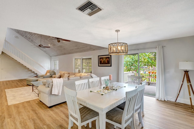 dining space with ceiling fan with notable chandelier, a wealth of natural light, lofted ceiling, and light hardwood / wood-style flooring