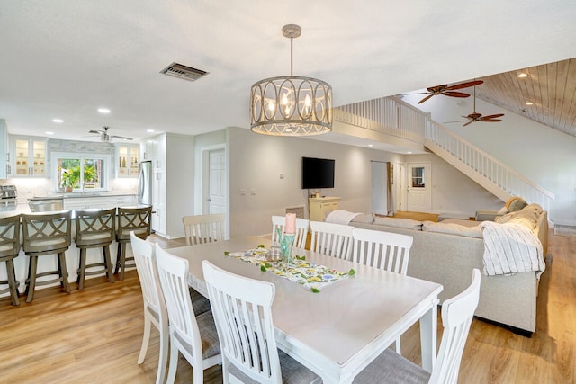 dining area with vaulted ceiling, sink, ceiling fan with notable chandelier, and light hardwood / wood-style floors