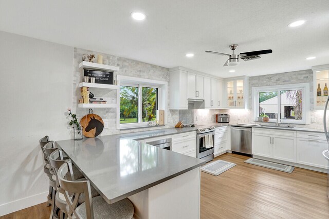 kitchen with light hardwood / wood-style floors, white cabinetry, kitchen peninsula, stainless steel appliances, and ceiling fan