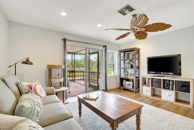 living room with light hardwood / wood-style floors, ceiling fan, and a textured ceiling