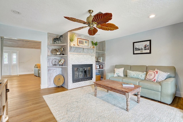 living room with a brick fireplace, wood-type flooring, ceiling fan, and a textured ceiling