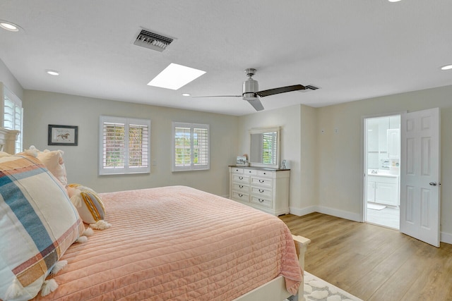 bedroom featuring ceiling fan, a skylight, ensuite bathroom, and light hardwood / wood-style floors