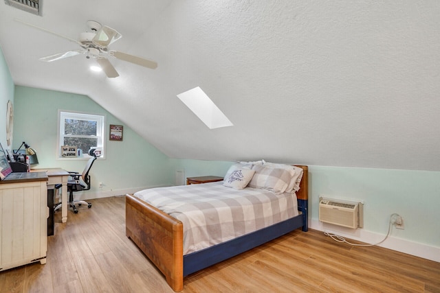 bedroom featuring light hardwood / wood-style floors, a textured ceiling, lofted ceiling with skylight, a wall mounted air conditioner, and ceiling fan