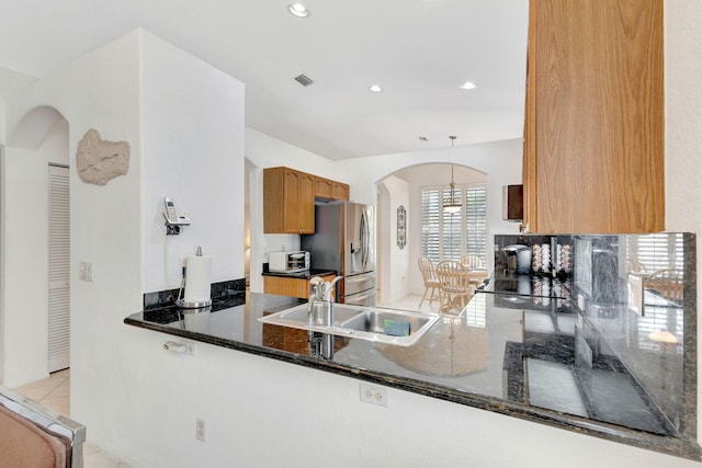 kitchen featuring sink, kitchen peninsula, black electric cooktop, stainless steel fridge, and dark stone counters