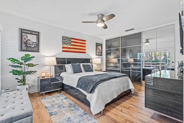 bedroom featuring a ceiling fan, a textured ceiling, visible vents, and wood finished floors