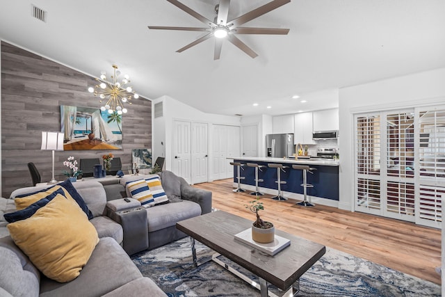 living room with lofted ceiling, light wood-style floors, visible vents, and wood walls