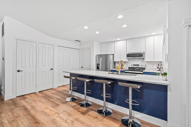 kitchen featuring a breakfast bar area, stainless steel appliances, a peninsula, white cabinets, and light countertops