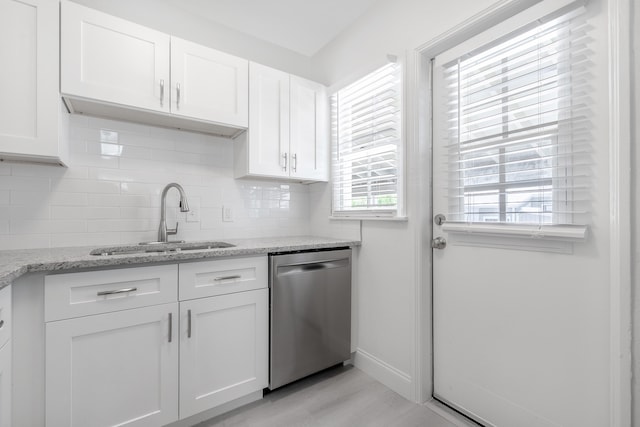 kitchen with stainless steel dishwasher, white cabinets, sink, light stone countertops, and backsplash