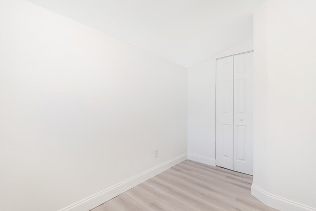 unfurnished bedroom featuring vaulted ceiling, a closet, and light wood-type flooring