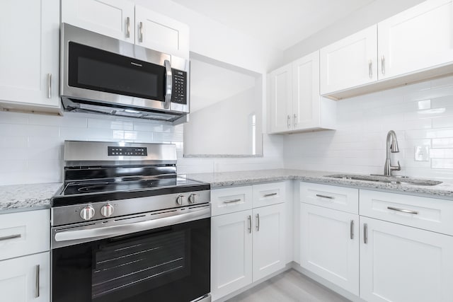 kitchen with appliances with stainless steel finishes, sink, decorative backsplash, light stone countertops, and white cabinetry