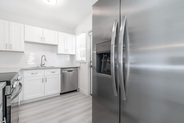 kitchen with appliances with stainless steel finishes, tasteful backsplash, white cabinets, sink, and light hardwood / wood-style floors