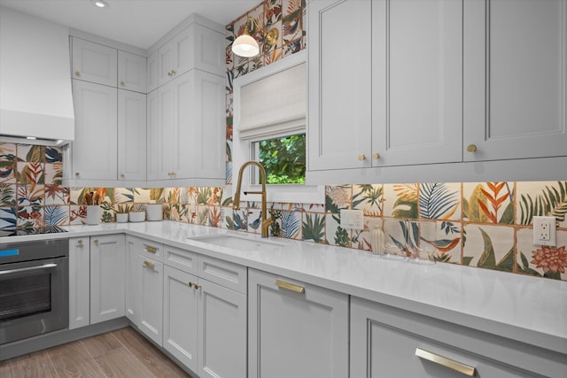 kitchen with backsplash, oven, premium range hood, light stone countertops, and white cabinets