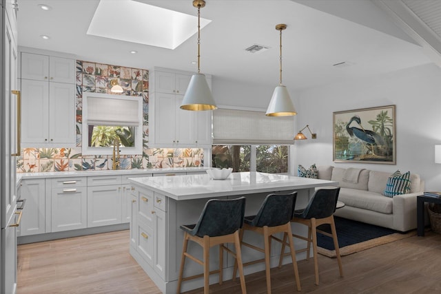 kitchen with tasteful backsplash, hanging light fixtures, a center island, light wood-type flooring, and white cabinets