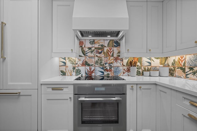 kitchen featuring custom range hood, white cabinetry, black electric cooktop, stainless steel oven, and tasteful backsplash