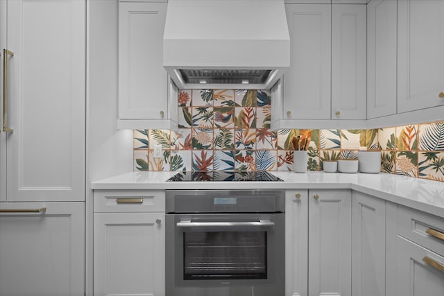 kitchen featuring premium range hood, white cabinets, light countertops, stainless steel oven, and decorative backsplash