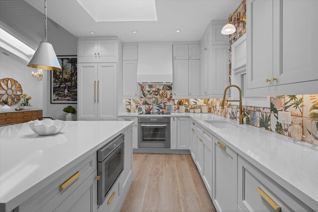 kitchen with light countertops, custom range hood, appliances with stainless steel finishes, a skylight, and a sink