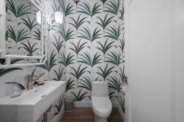 bathroom featuring wallpapered walls, baseboards, toilet, wood finished floors, and a sink