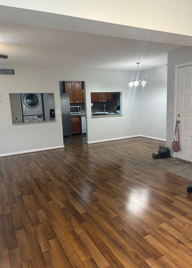 unfurnished living room with a textured ceiling, stacked washing maching and dryer, dark hardwood / wood-style floors, and a chandelier