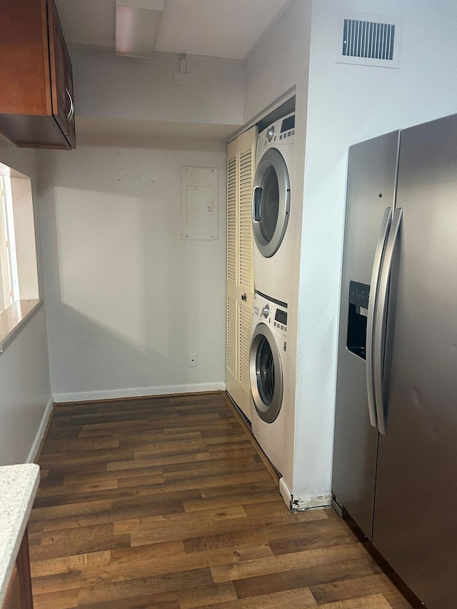 laundry room featuring electric panel, stacked washer and dryer, and dark hardwood / wood-style floors