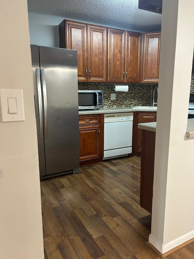 kitchen featuring a textured ceiling, dark hardwood / wood-style floors, appliances with stainless steel finishes, tasteful backsplash, and sink