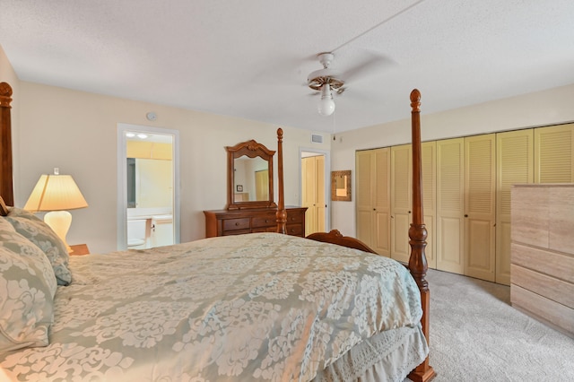 carpeted bedroom with multiple closets, a textured ceiling, ensuite bathroom, and ceiling fan