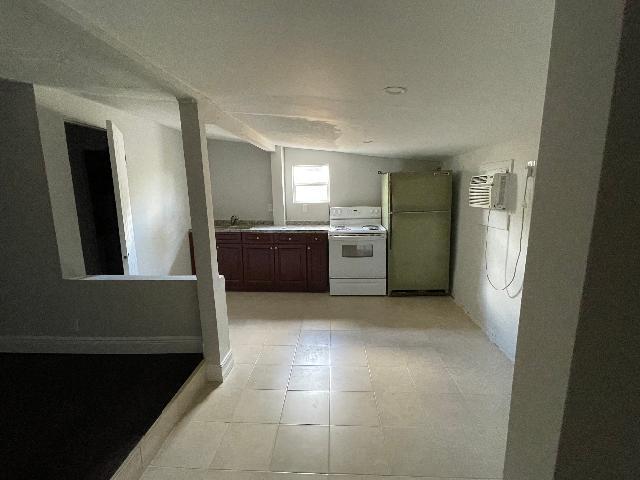 kitchen with a wall mounted air conditioner, light tile patterned flooring, lofted ceiling, and white appliances