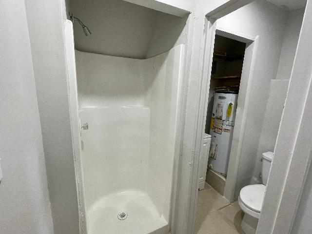 bathroom with a shower, water heater, and toilet