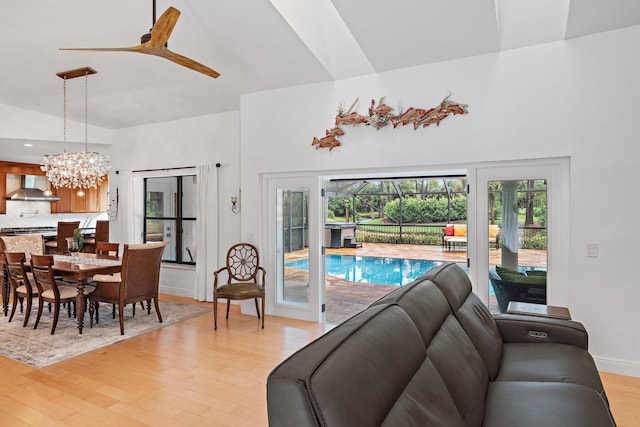 living room with ceiling fan with notable chandelier, vaulted ceiling, and light hardwood / wood-style flooring